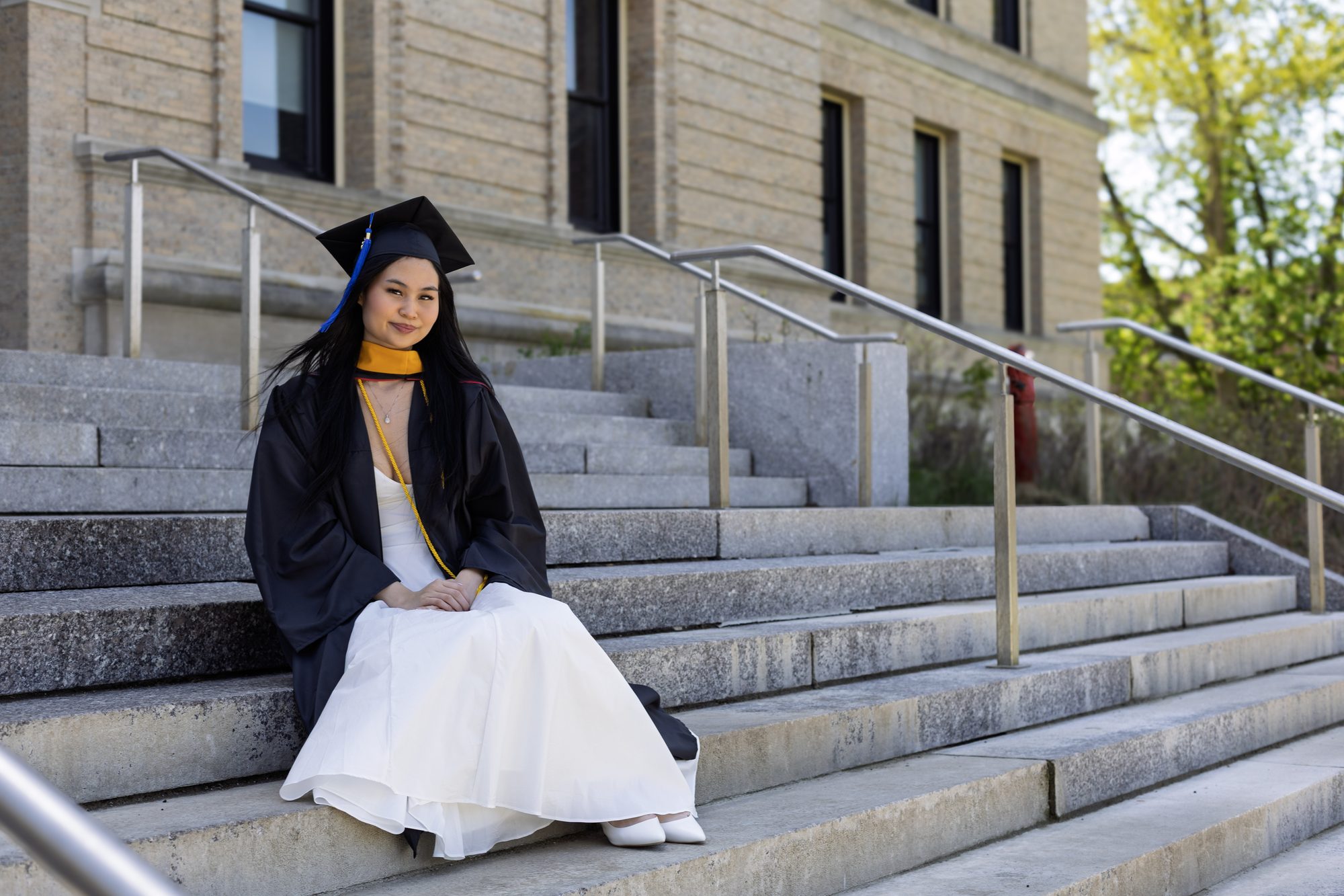 Graduate in cap and gown seated on wide stone steps outside a campus building