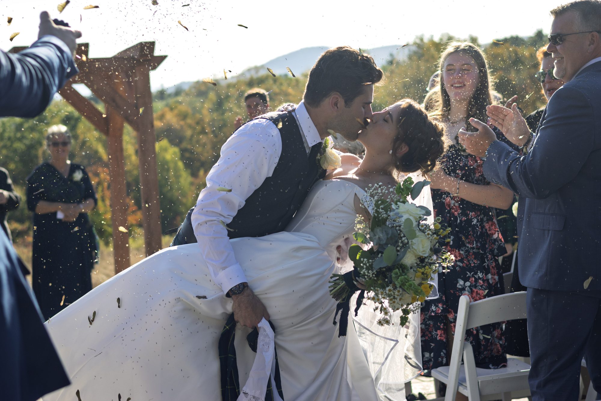 Groom dipping the bride for a kiss as guests cheer and toss confetti after the ceremony