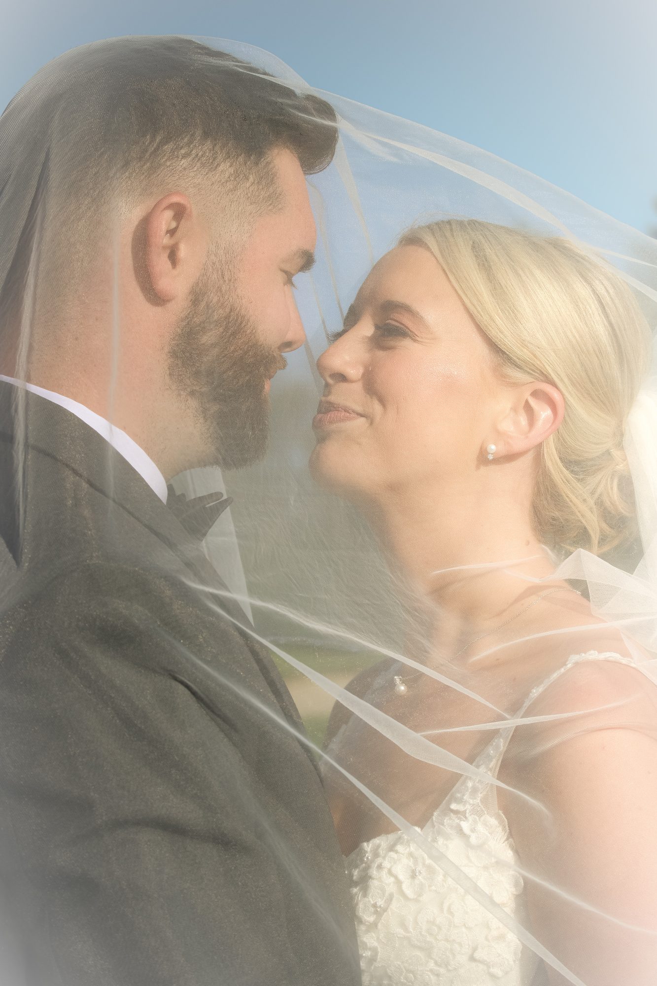 Close portrait of a bride and groom nose to nose beneath a sunlit veil